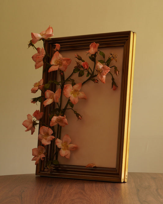 Framed floral arrangement on a wooden surface with a pale pink background