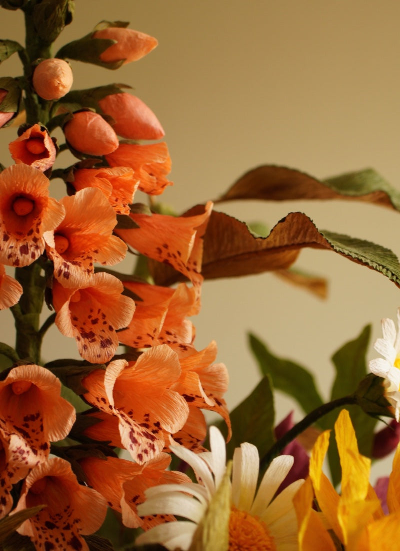 Cluster of handcrafted paper foxglove flowers in warm orange tones, arranged with layered petals and botanical detail