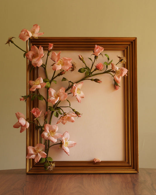 Framed pink floral arrangement on a wooden surface with a neutral background