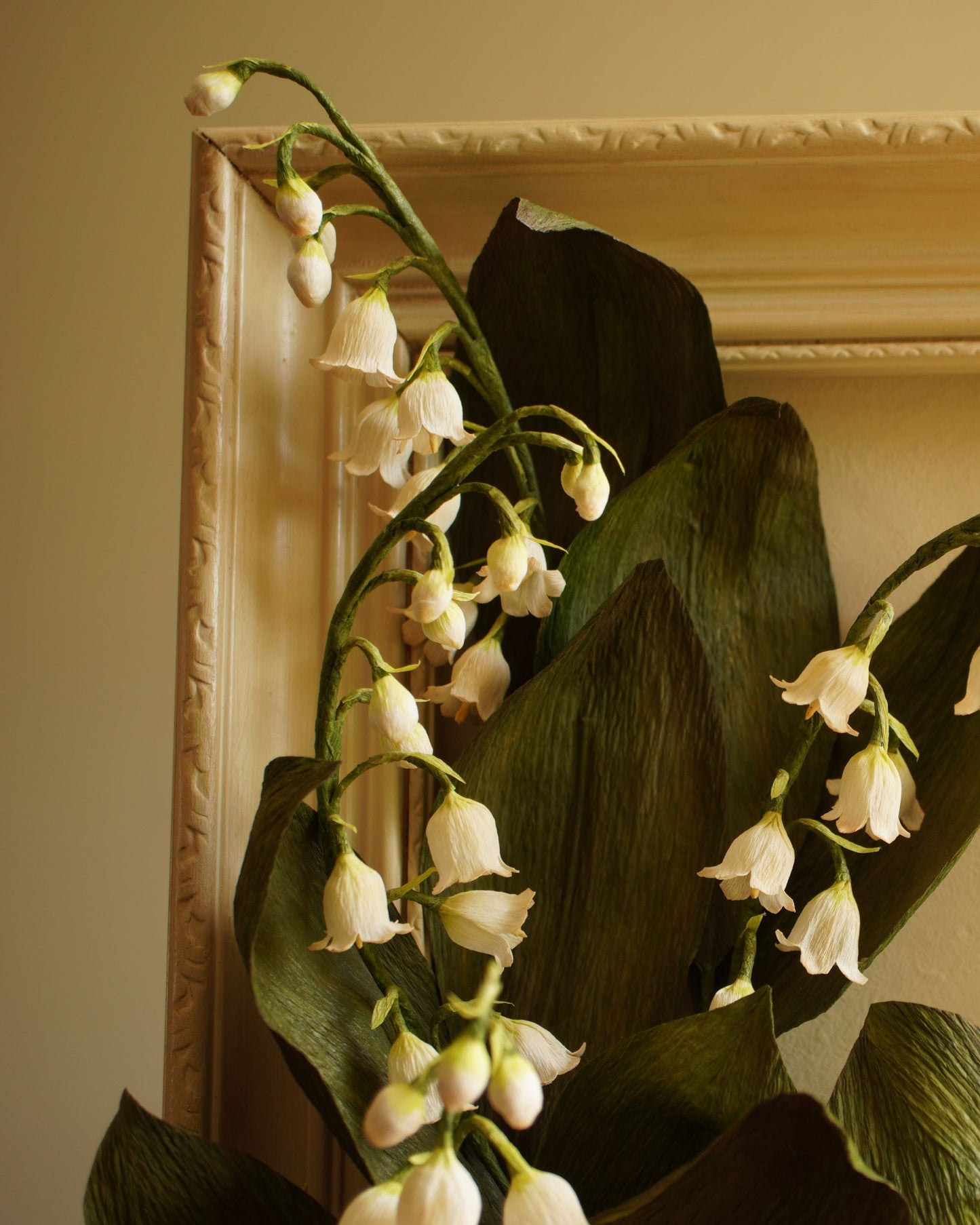Close up of paper lily of the valley flowers resting against the frame, highlighting texture, form and natural movement