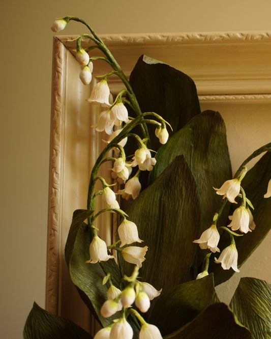 Close up of paper lily of the valley flowers resting against the frame, highlighting texture, form and natural movement