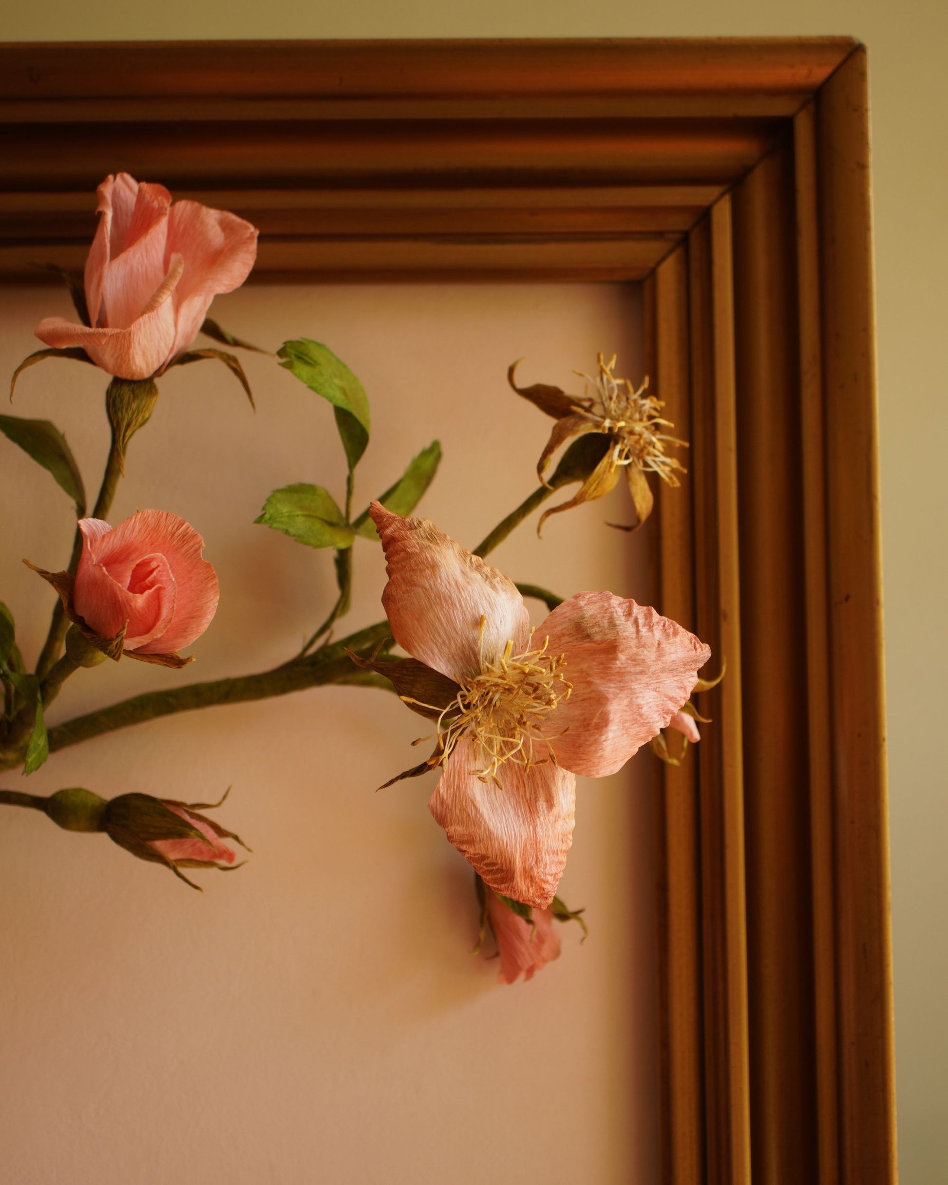 Detail of paper roses and buds positioned against the inner edge of a wooden frame