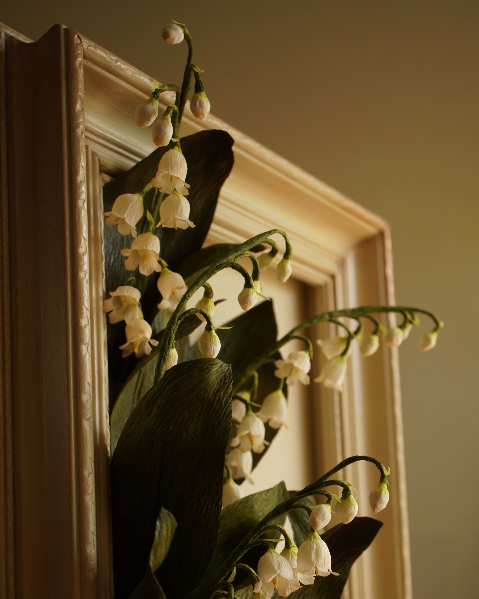 Angled view of framed paper lily of the valley artwork, showing flowers extending forward with sculptural depth from the frame