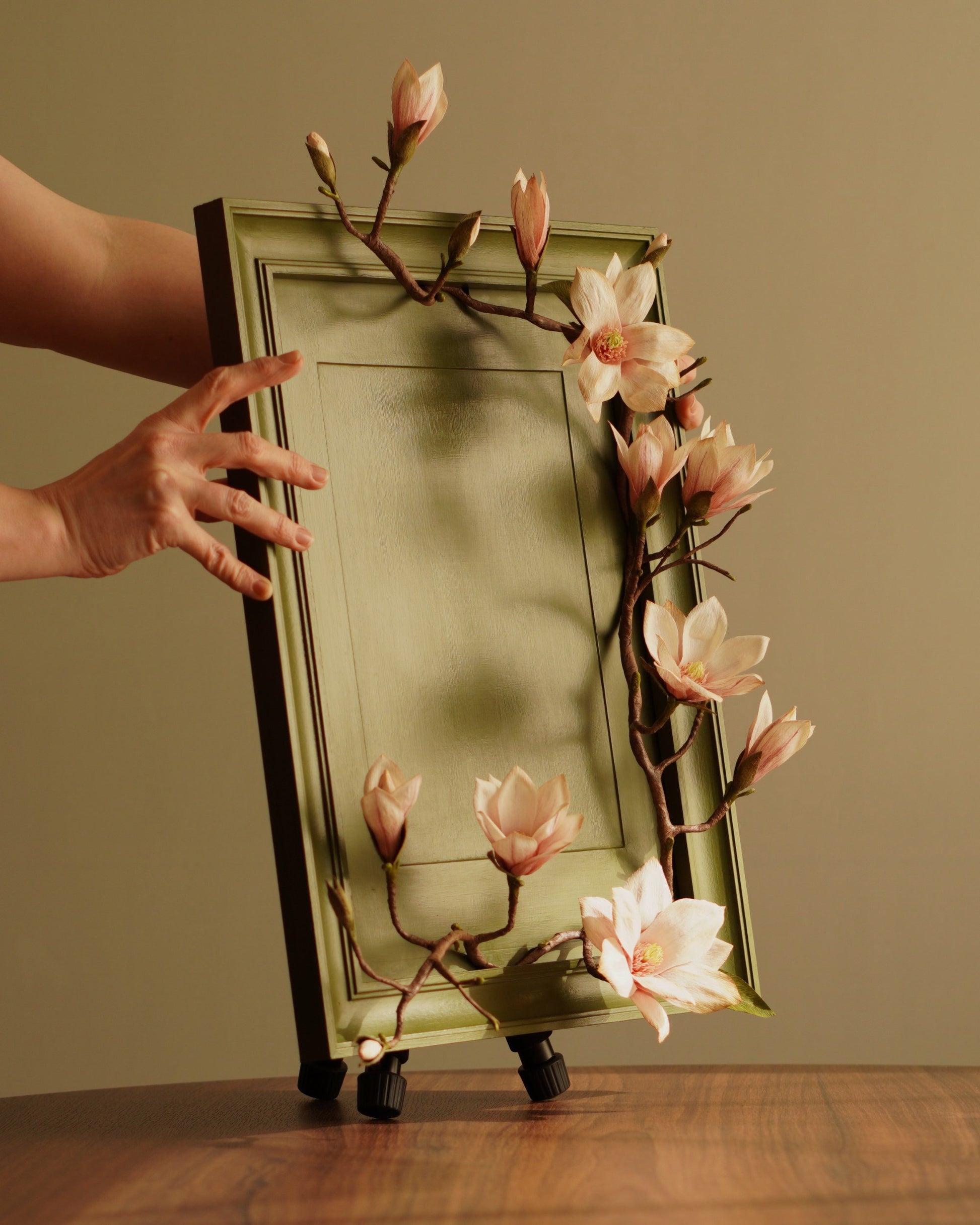 Hand holding framed magnolia artwork showing scale and structure of piece