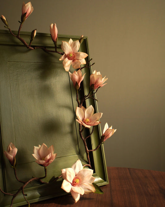 Angled view of framed magnolia artwork showing branch extending across and beyond frame