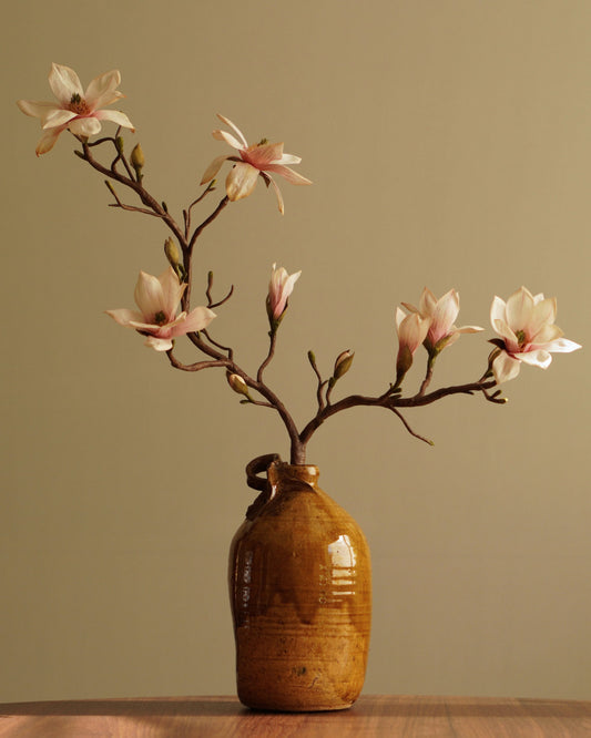 Paper magnolia branch with multiple blooms and buds arranged in ceramic vase on wooden surface