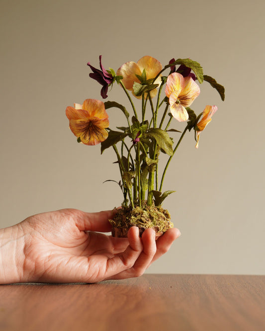 Hand holding yellow and purple paper pansy botanical sculpture showing scale and base