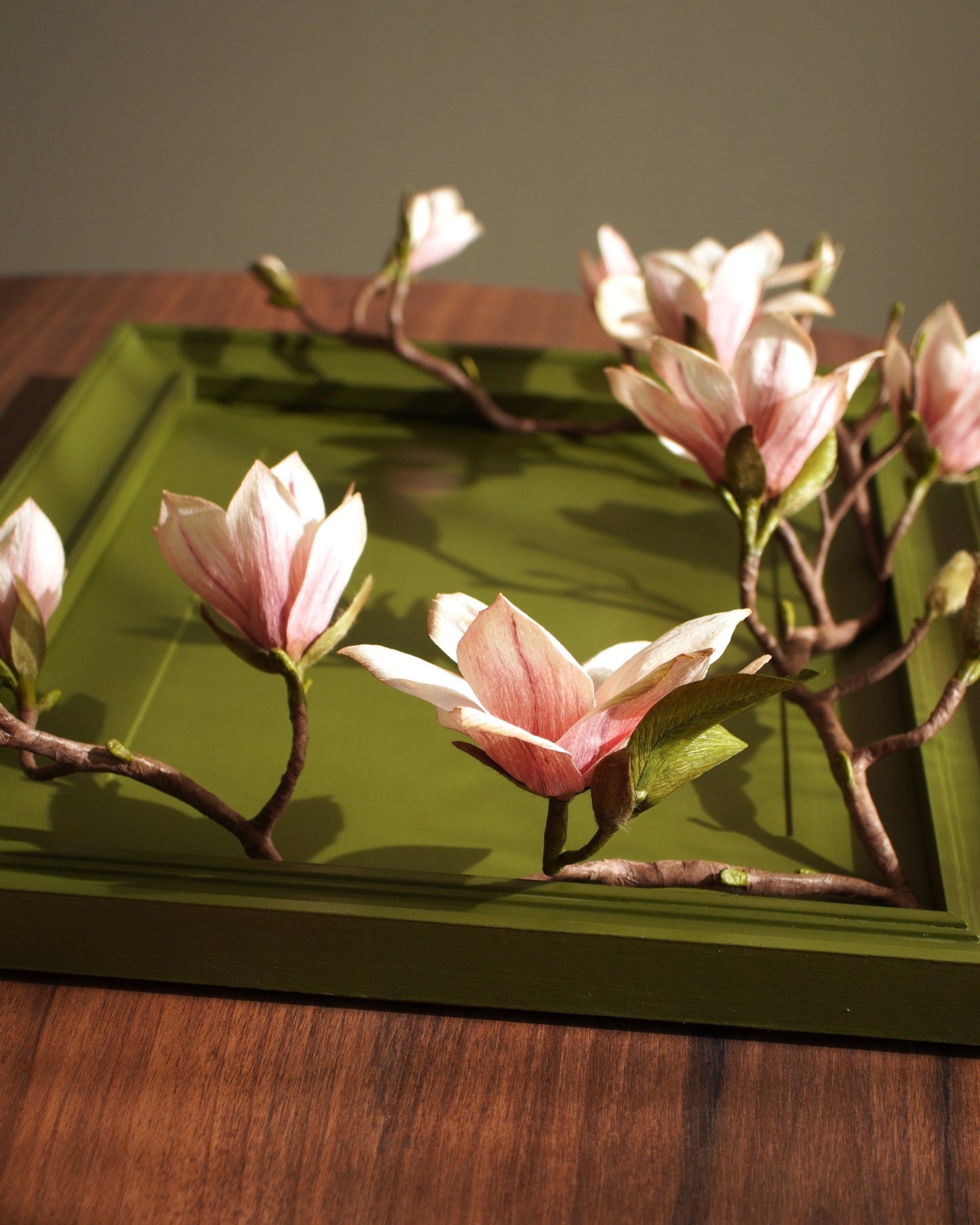 Paper magnolia flowers arranged across painted frame showing surface and depth
